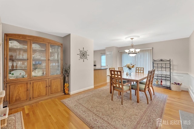 dining space featuring a wainscoted wall, light wood finished floors, and a notable chandelier