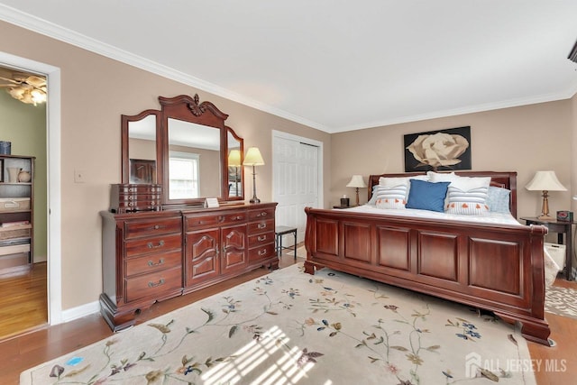 bedroom with crown molding, light wood-style flooring, baseboards, and a closet