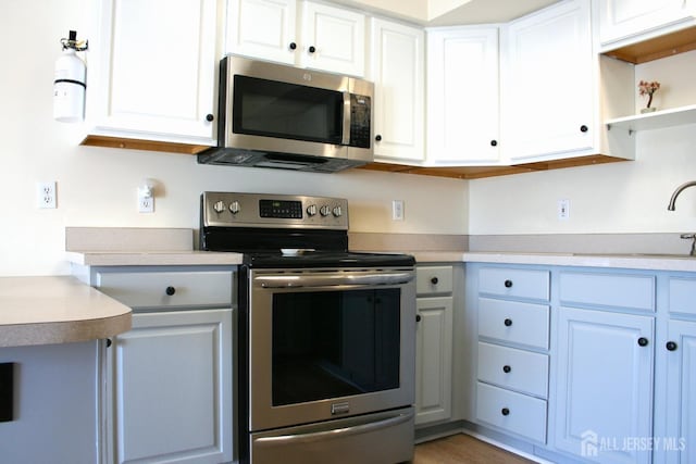 kitchen with appliances with stainless steel finishes, light countertops, a sink, white cabinetry, and open shelves