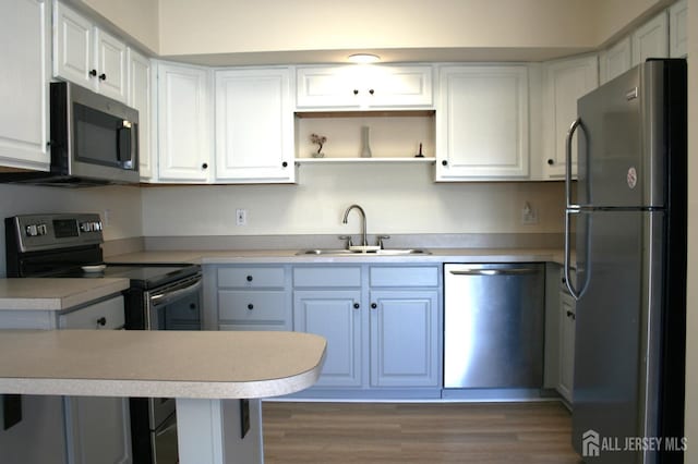 kitchen with appliances with stainless steel finishes, a sink, white cabinetry, light countertops, and wood finished floors