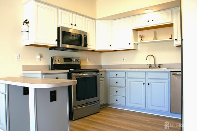 kitchen with appliances with stainless steel finishes, a peninsula, a sink, open shelves, and light countertops