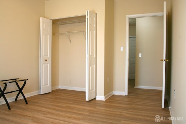 unfurnished bedroom featuring light wood-style floors, baseboards, and a closet