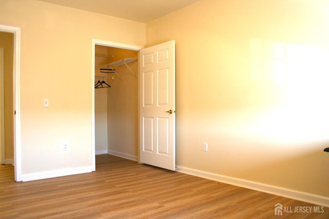 unfurnished bedroom featuring light wood finished floors, baseboards, and a closet
