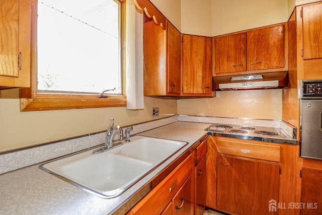 kitchen featuring brown cabinets, a sink, under cabinet range hood, electric cooktop, and stainless steel oven