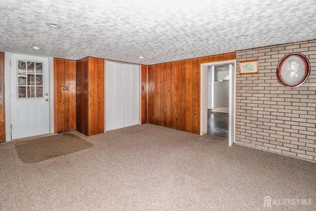 interior space featuring carpet floors, wood walls, and brick wall