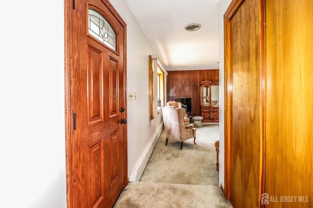 corridor featuring baseboards, wooden walls, and light carpet