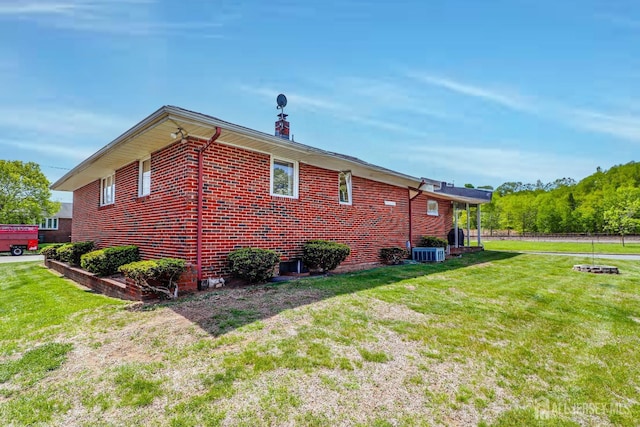 view of side of home with a lawn, central AC unit, and brick siding