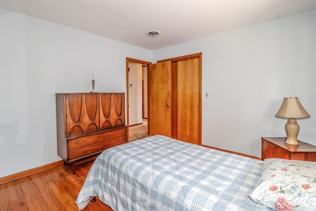 bedroom featuring baseboards, wood finished floors, visible vents, and a closet