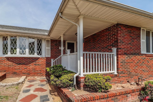 view of exterior entry with brick siding and covered porch