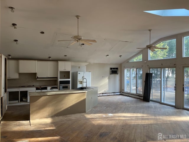 kitchen featuring white cabinets, stainless steel oven, ceiling fan, an island with sink, and white fridge with ice dispenser