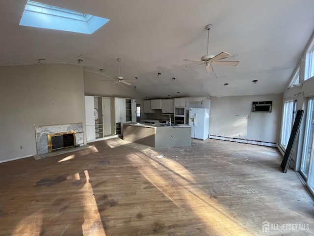 unfurnished living room with ceiling fan, a premium fireplace, a skylight, a sink, and an AC wall unit