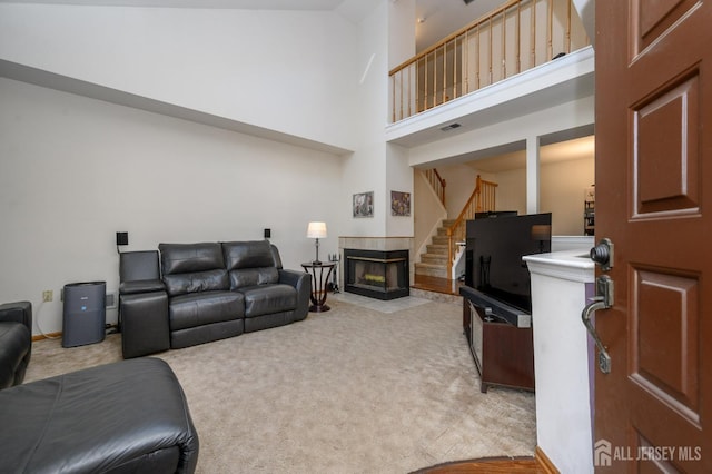 living area featuring visible vents, a towering ceiling, light carpet, a tile fireplace, and stairs