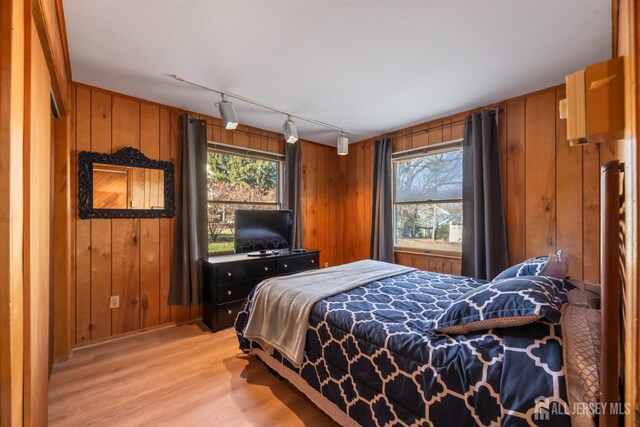 bedroom featuring light hardwood / wood-style floors, multiple windows, and wood walls