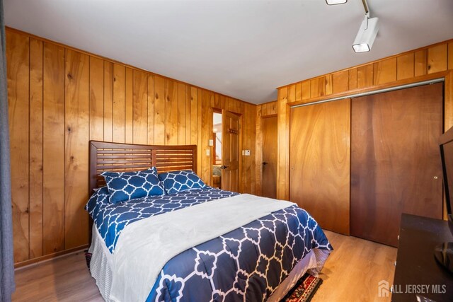 bedroom featuring wooden walls, light wood-type flooring, and a closet