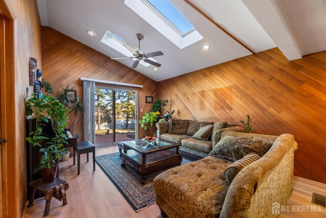 living room with a skylight, light wood-type flooring, wooden walls, beamed ceiling, and ceiling fan