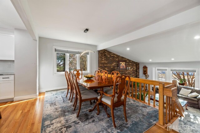 dining room with brick wall, plenty of natural light, lofted ceiling with beams, and light hardwood / wood-style flooring