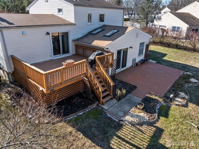 rear view of house with a wooden deck, a patio, and a lawn