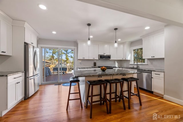 kitchen featuring white cabinetry, decorative light fixtures, stainless steel appliances, and a kitchen island