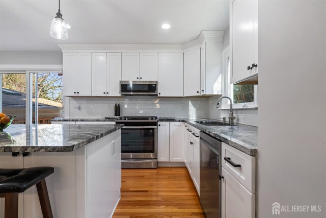 kitchen with a breakfast bar, sink, white cabinetry, decorative light fixtures, and appliances with stainless steel finishes