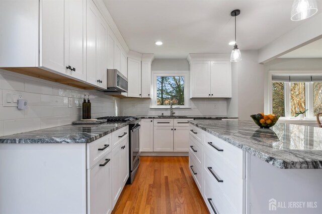 kitchen featuring sink, light hardwood / wood-style flooring, hanging light fixtures, appliances with stainless steel finishes, and white cabinets