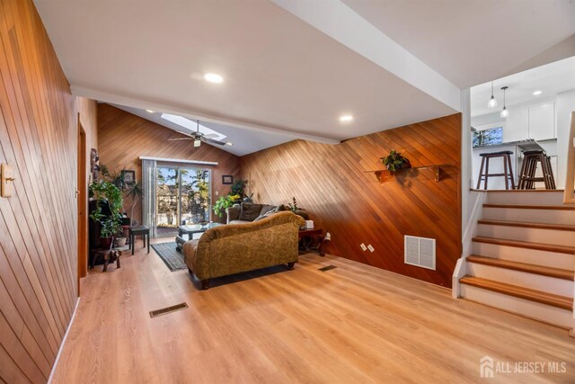 living room featuring vaulted ceiling, ceiling fan, light hardwood / wood-style floors, and wood walls