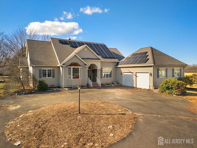 view of front of property featuring driveway, solar panels, an attached garage, a shingled roof, and entry steps