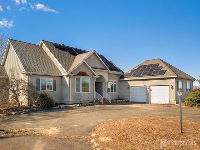 view of front of home featuring a garage, solar panels, concrete driveway, and a shingled roof