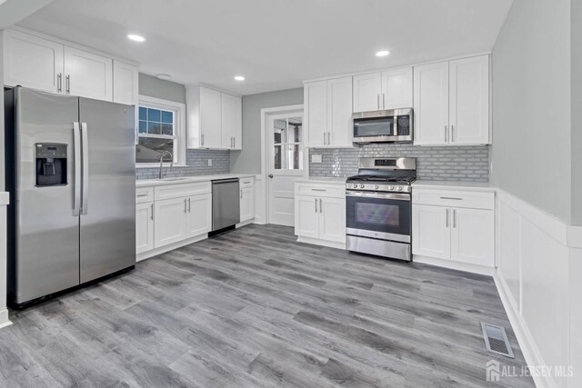 kitchen with backsplash, white cabinetry, stainless steel appliances, and light wood-type flooring