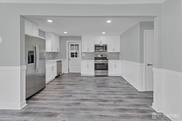 kitchen with tasteful backsplash, white cabinets, stainless steel appliances, and light wood-type flooring