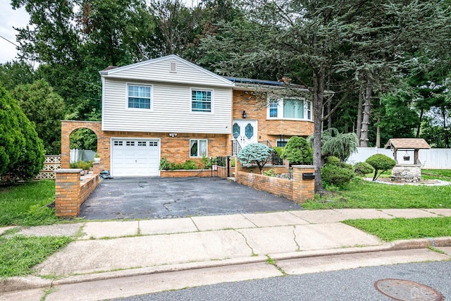 bi-level home with a garage, brick siding, driveway, and fence