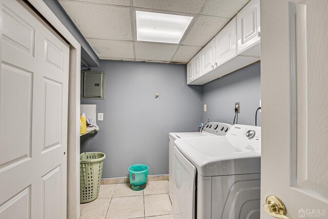 clothes washing area featuring light tile patterned flooring, electric panel, washing machine and clothes dryer, and cabinets