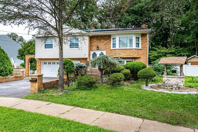 split foyer home with brick siding, an attached garage, a front yard, a chimney, and driveway