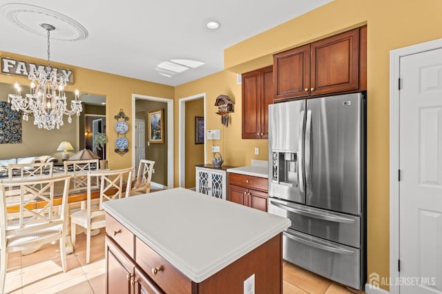 kitchen with stainless steel refrigerator with ice dispenser, decorative light fixtures, a kitchen island, light countertops, and light tile patterned floors