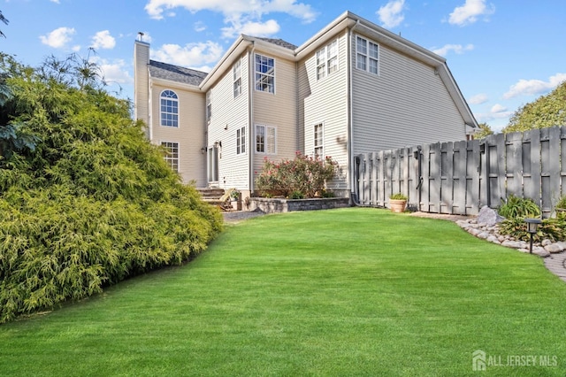 back of property featuring a yard, fence, and a chimney