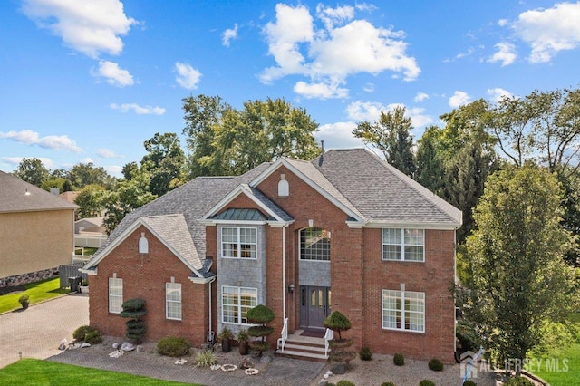 view of front of house with central air condition unit, brick siding, and roof with shingles