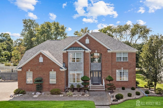 view of front of house featuring fence, brick siding, and roof with shingles