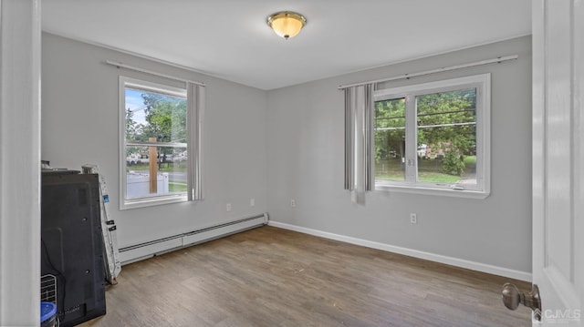 unfurnished room featuring a healthy amount of sunlight, hardwood / wood-style floors, and baseboard heating