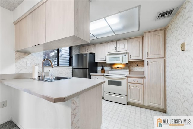 kitchen featuring light countertops, visible vents, a sink, white appliances, and a peninsula