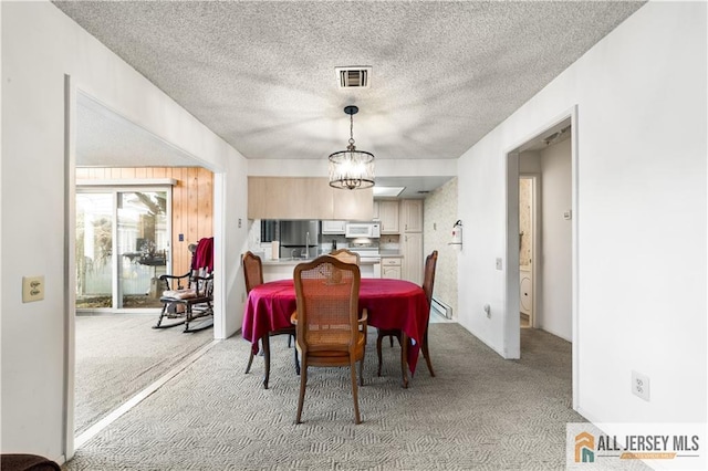 dining room with carpet floors, a textured ceiling, visible vents, and a notable chandelier