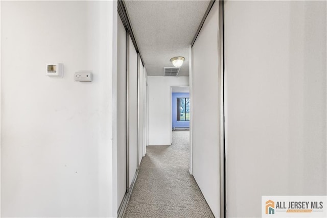 hallway with light carpet, a textured ceiling, and visible vents