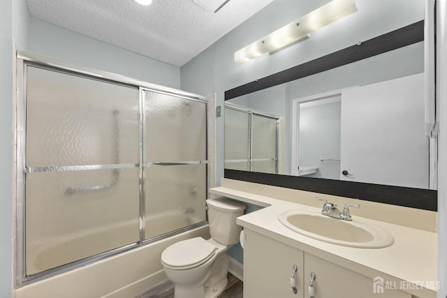 full bathroom featuring toilet, shower / bath combination with glass door, a textured ceiling, and vanity