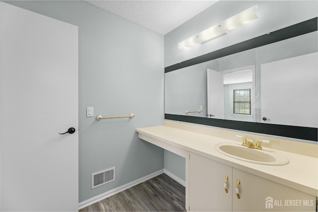 bathroom featuring a textured ceiling, wood finished floors, vanity, visible vents, and baseboards