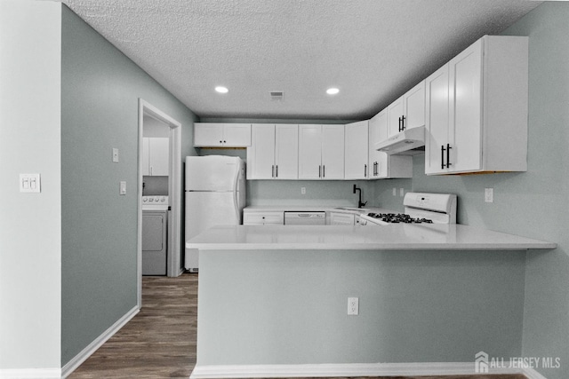 kitchen featuring under cabinet range hood, white appliances, a sink, light countertops, and washer / clothes dryer