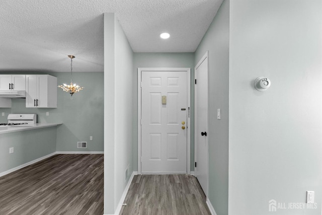 foyer entrance with visible vents, a textured ceiling, wood finished floors, a chandelier, and baseboards