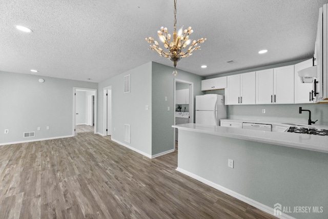 kitchen with light countertops, white appliances, visible vents, and wall chimney range hood