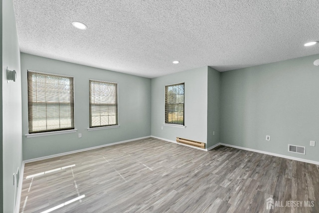 spare room featuring baseboard heating, wood finished floors, visible vents, and a healthy amount of sunlight