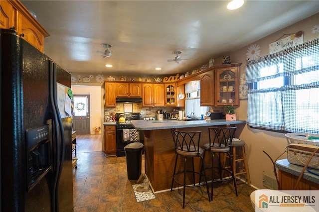 7 Cornell Rd, Old Bridge, NJ 08859 - kitchen featuring black appliances, under cabinet range hood, a peninsula, brown cabinets, and glass insert cabinets