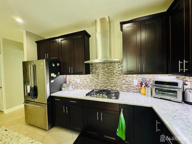 kitchen featuring wall chimney exhaust hood, tasteful backsplash, light stone counters, light tile patterned floors, and stainless steel appliances
