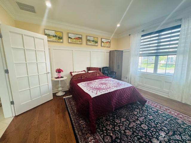 bedroom featuring visible vents, crown molding, a decorative wall, and wood finished floors