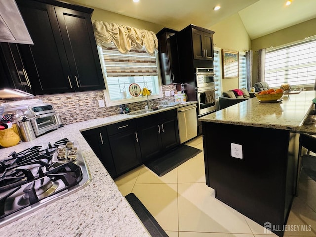 kitchen featuring appliances with stainless steel finishes, tasteful backsplash, vaulted ceiling, a sink, and dark cabinetry